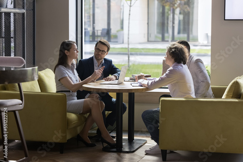 Serious millennial team of professionals, four businesspeople negotiating in modern office, discuss project, consider contract terms and conditions, solve business, take part in formal meeting event