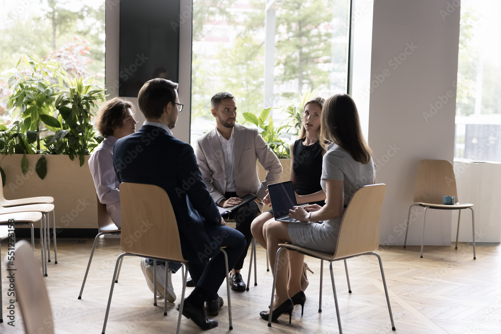 Office employees gathered for morning briefing, gain information or instructions, discuss new project, sales results seated on chairs in circle in modern workspace. Business seminar or training event