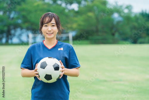 サッカーボールを持ちながらフットサル・サッカー場に立つ笑顔のファン・サポーター・選手の日本人女性  © buritora