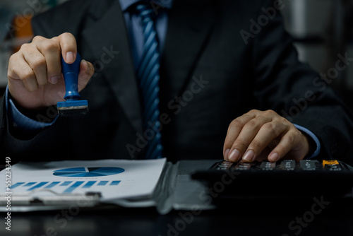 Business person holding stamp rubber approve on document contract and finance on desk.