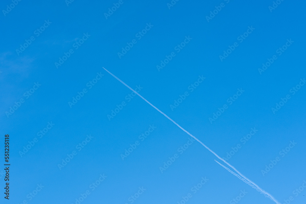 A plane flying high in the sky leaving a white trail on a blue cloudless sky. Travel concept. Bright blue sky gradient background. Cloudless empty sky. Natural background A plane flying high in the sky leaving a white trail on a blue cloudless sky. Travel concept. Bright blue sky gradient background. Cloudless empty sky. Natural background