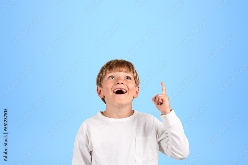 Happy boy with finger pointing up on copy space blue background Happy boy with finger pointing up on copy space blue background