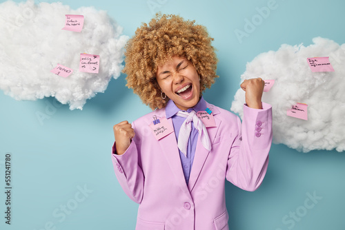 фотографія Overjoyed female entrepreneur with curly blonde hair dressed formally clenches f