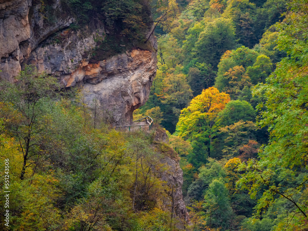 Walking path around the mountain covered with green mixed forest. North Ossetia, Alagir Gorge. Dangerous path around the cliff.