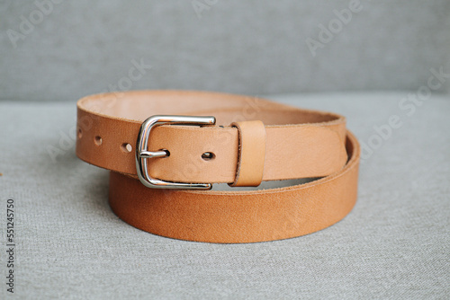 Beige traitional faux leather belt coiled in two loops on a gray fabric surface. photo