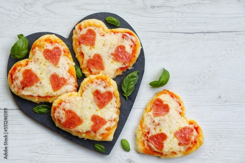 Heart shaped mini pizzas with heart shaped pepperoni on heart shaped slate plate with white wood background.Creative art food idea for celebrate Valentine or Mother day.Top view.Copy space