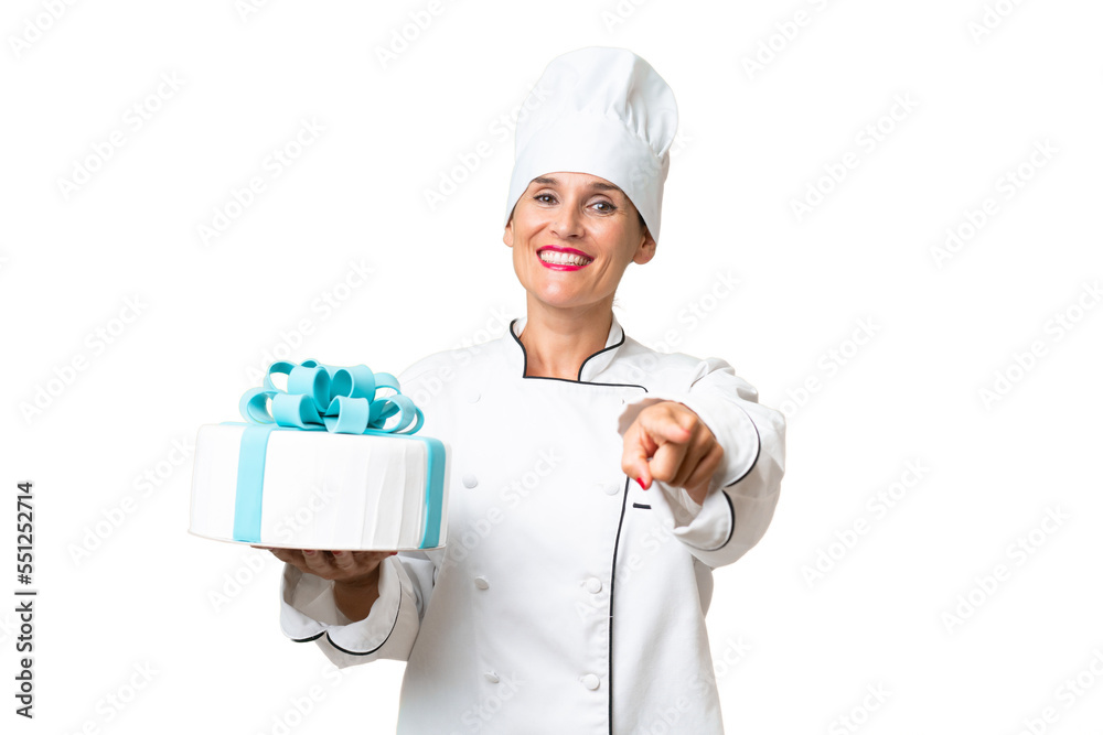 Middle-aged chef caucasian woman with a big cake over isolated background points finger at you with a confident expression Middle-aged chef caucasian woman with a big cake over isolated background points finger at you with a confident expression