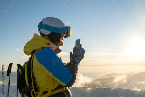 woman skier taking picture of sunset above the mountains