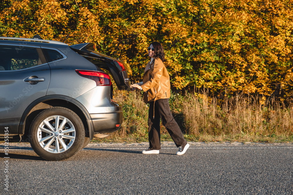 After a ride through the autumn forest, the woman closes the trunk of her car After a ride through the autumn forest, the woman closes the trunk of her car