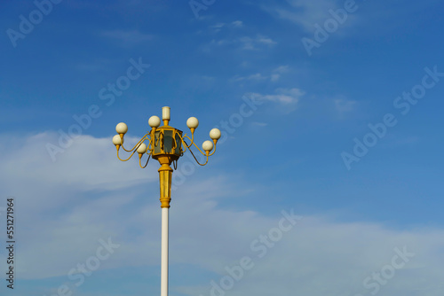 Vintage street lamp against blue sky with white clouds.