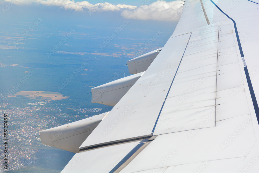View from an airplane window showing the wing, sky, clouds and land