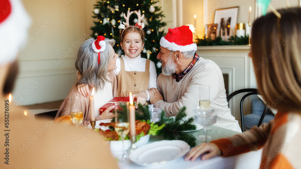 Loving senior grandparents give Christmas gift to happy girl granddaughter during festive dinner Loving senior grandparents give Christmas gift to happy girl granddaughter during festive dinner