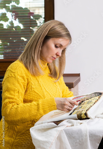 Photography Beautiful Caucasian woman sitting at table and cross stitching big multicolor pi