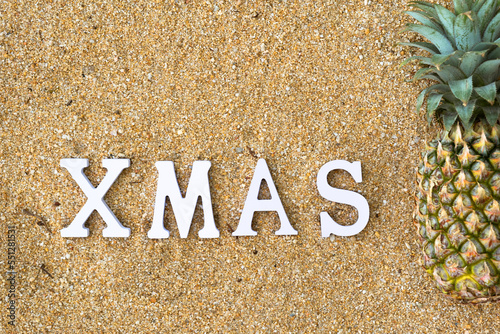 Lettering XMAS on yellow sand with pineapple. Tropical christmas celebration concept. Top view