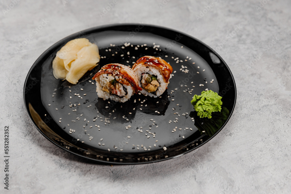 Two servings of shrimp and eel sushi with vossabi sauce and ginger on a black plate