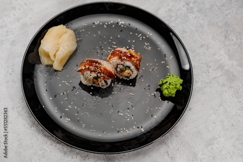 Two servings of shrimp and eel sushi with vossabi sauce and ginger on a black plate