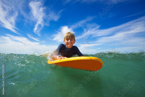 Happy boy swim on surf board smiling and looking at camera