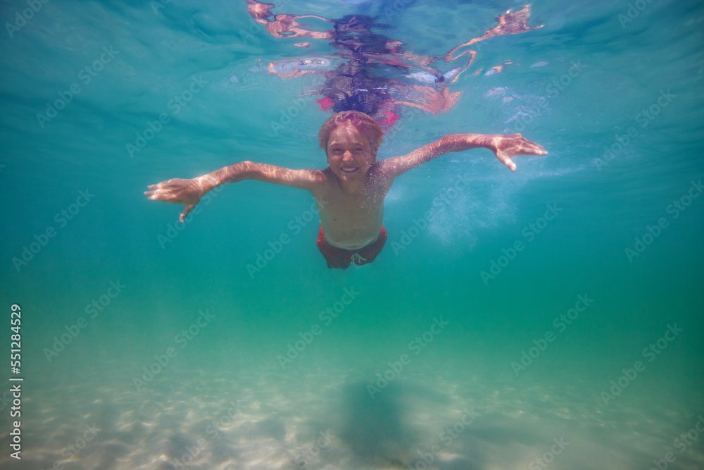 Smiling boy swim underwater in the ocean with open eyes