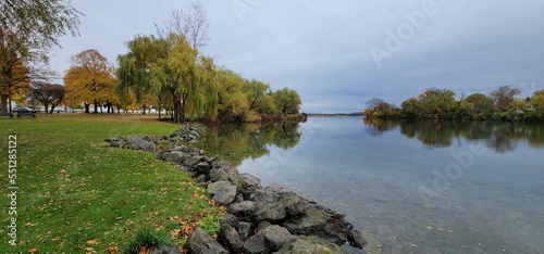 Calm water pond at Kingsbridge Park with autumn trees in the background on a cloudy day