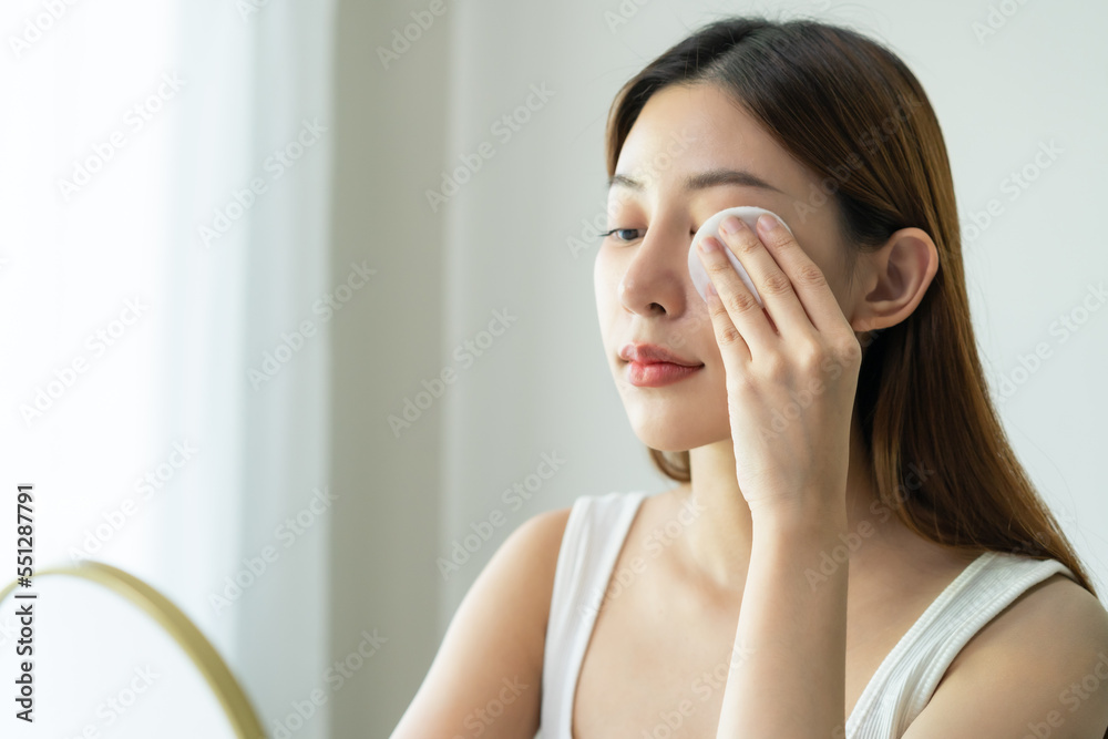 Fototapeta premium Relax beauty, attractive asian young woman, girl close eyes looking in mirror, hand holding cotton pad, apply facial wipe on her face remover makeup, essence or lotion for treatment, skin care routine