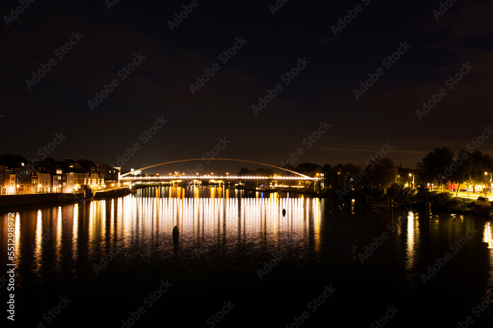 Cityscape with a bridge over the river Meuse of the center of Maastricht at night in the Netherlands