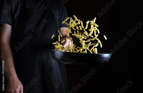 Cooking vegetarian food with noodles and vegetables in a restaurant. The cook throws food into a hot pan. Place for advertising on a black background