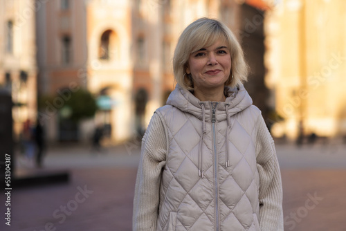 Portrait of Caucasian adult happy blonde woman in jacket posing in city centre. Concept of carefree and psychology © _KUBE_