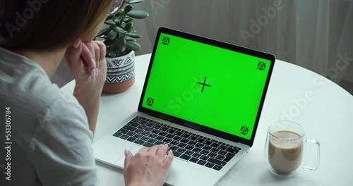 Unrecognizable woman using chromakey screen laptop computer sitting at table with coffee at home, over shoulder view