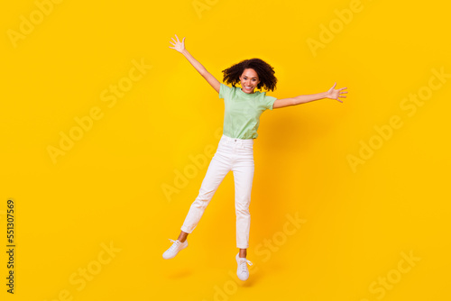 Full length photo of young gorgeous nice pretty girl wear casual clothes beaming palms up jump dance celebrate party weekend isolated on yellow color background