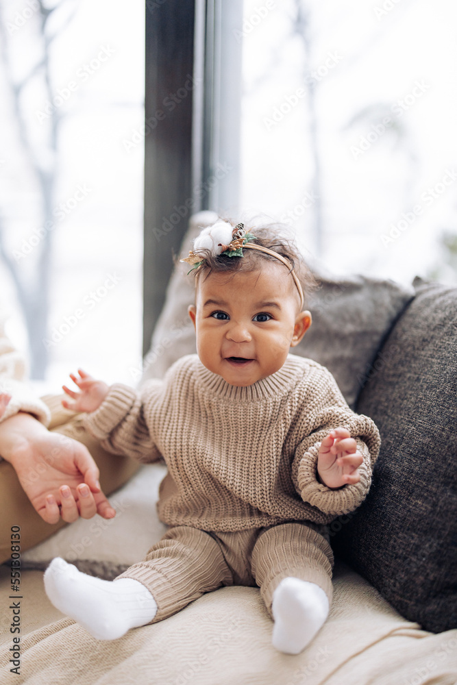 Happy mixed race baby girl sits near pillows against window. Happy mixed race baby girl sits near pillows against window.