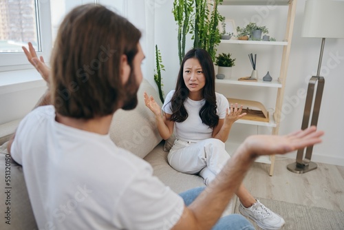 A man and a woman sit on the couch at home in white T-shirts and shouting communicate scandalously do not understand each other. A quarrel in the family of two spouses and aggression, sad emotions