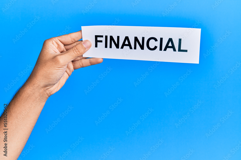 Hand of caucasian man holding paper with financial word over isolated blue background Hand of caucasian man holding paper with financial word over isolated blue background