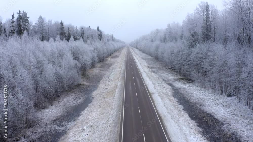 Flying forward directly on a drone over a road with a forest with trees covered with snow and hoarfrost in early winter Flying forward directly on a drone over a road with a forest with trees covered with snow and hoarfrost in early winter