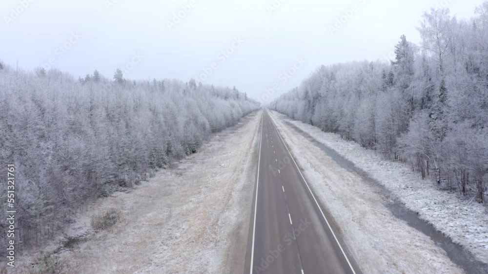 Flying forward directly on a drone over a road with a forest with trees covered with snow and hoarfrost in early winter Flying forward directly on a drone over a road with a forest with trees covered with snow and hoarfrost in early winter