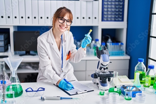 Young woman scientist holding test tube write on clipboard at laboratory