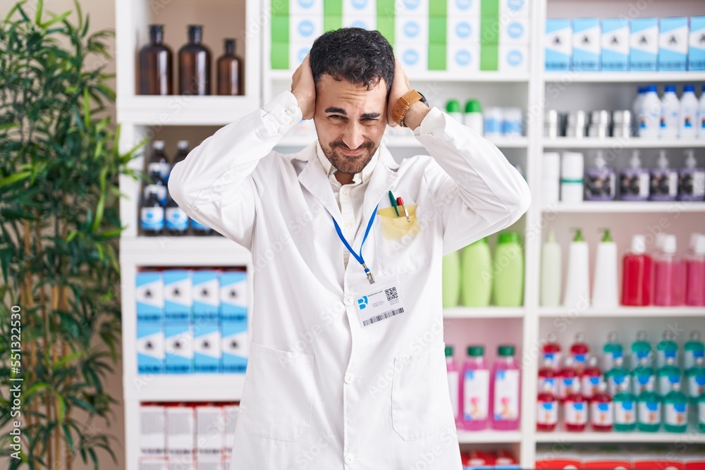 Handsome hispanic man working at pharmacy drugstore suffering from headache desperate and stressed because pain and migraine. hands on head.