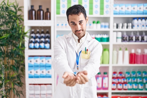 Handsome hispanic man working at pharmacy drugstore smiling with hands palms together receiving or giving gesture. hold and protection © Krakenimages.com