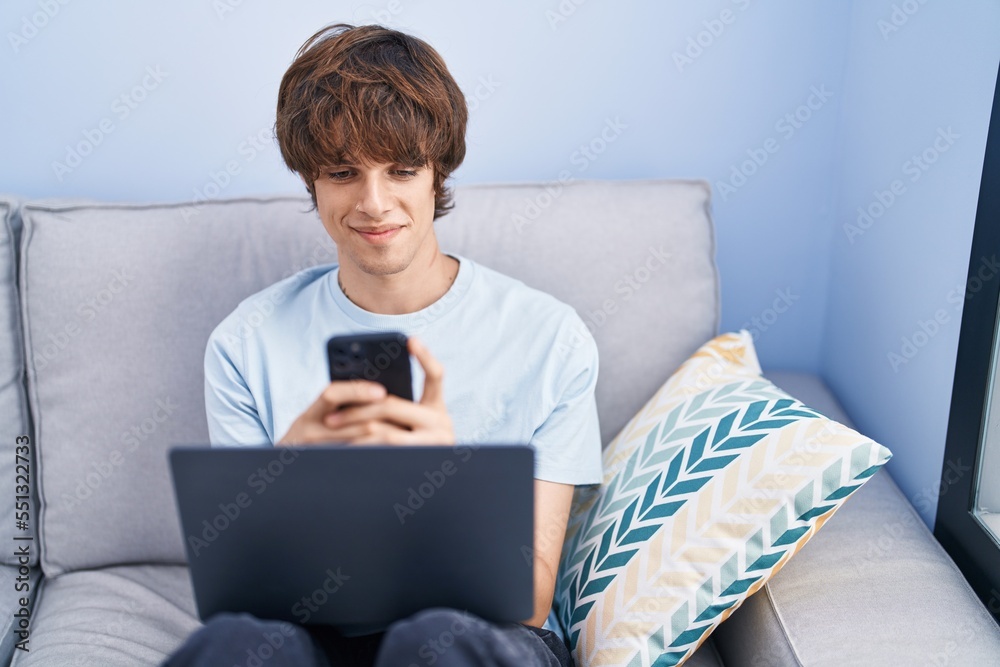 Young blond man using smartphone and laptop at home Young blond man using smartphone and laptop at home