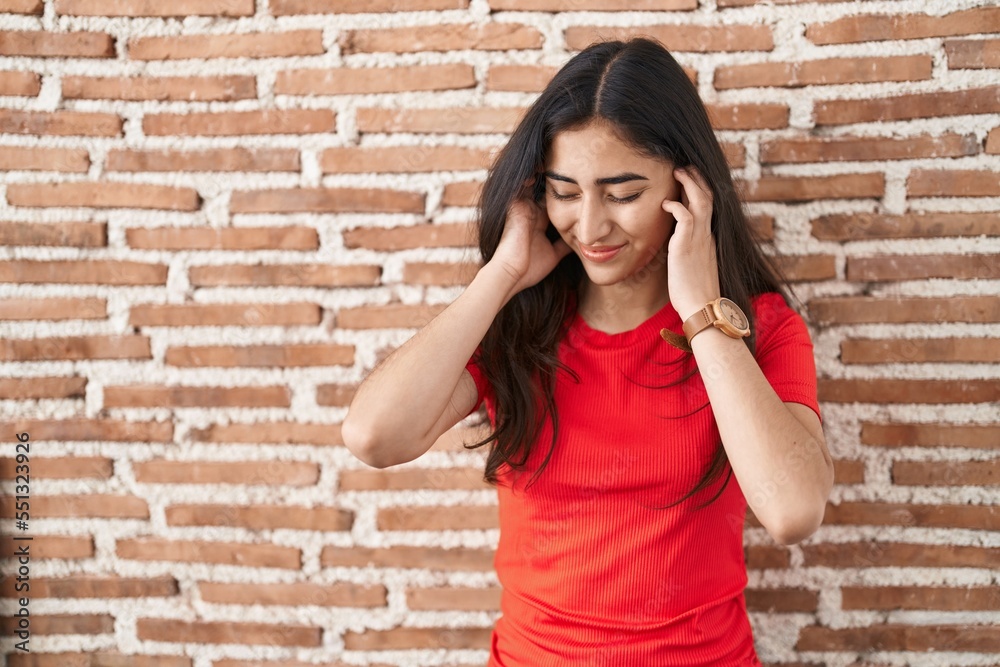 Young teenager girl standing over bricks wall covering ears with fingers with annoyed expression for the noise of loud music. deaf concept. Young teenager girl standing over bricks wall covering ears with fingers with annoyed expression for the noise of loud music. deaf concept.