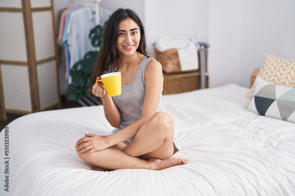 Young hispanic girl drinking cup of coffee sitting on bed at bedroom Young hispanic girl drinking cup of coffee sitting on bed at bedroom