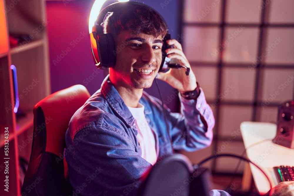 Young hispanic man streamer smiling confident sitting on table at gaming room Young hispanic man streamer smiling confident sitting on table at gaming room