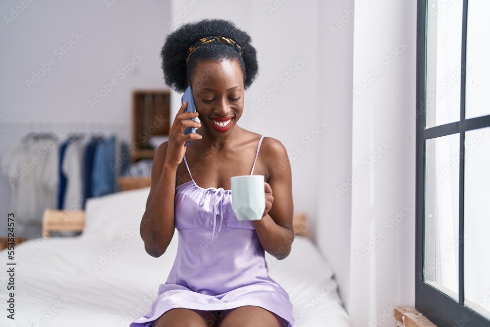 African american woman alking on smartphone drinking coffee at bedroom