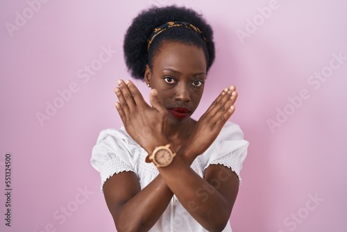 African woman with curly hair standing over pink background rejection expression crossing arms doing negative sign, angry face
