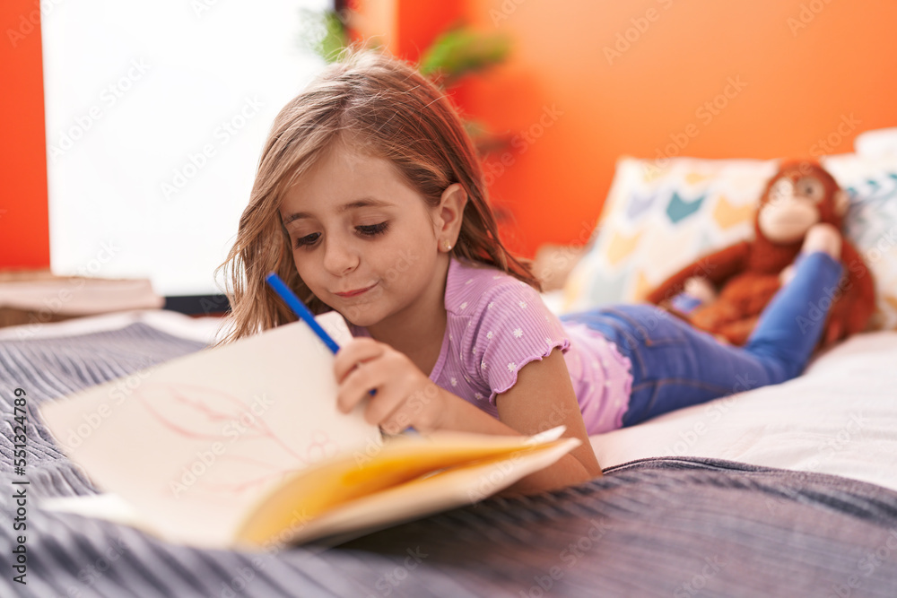 Adorable hispanic girl writing on notebook lying on bed at bedroom Adorable hispanic girl writing on notebook lying on bed at bedroom