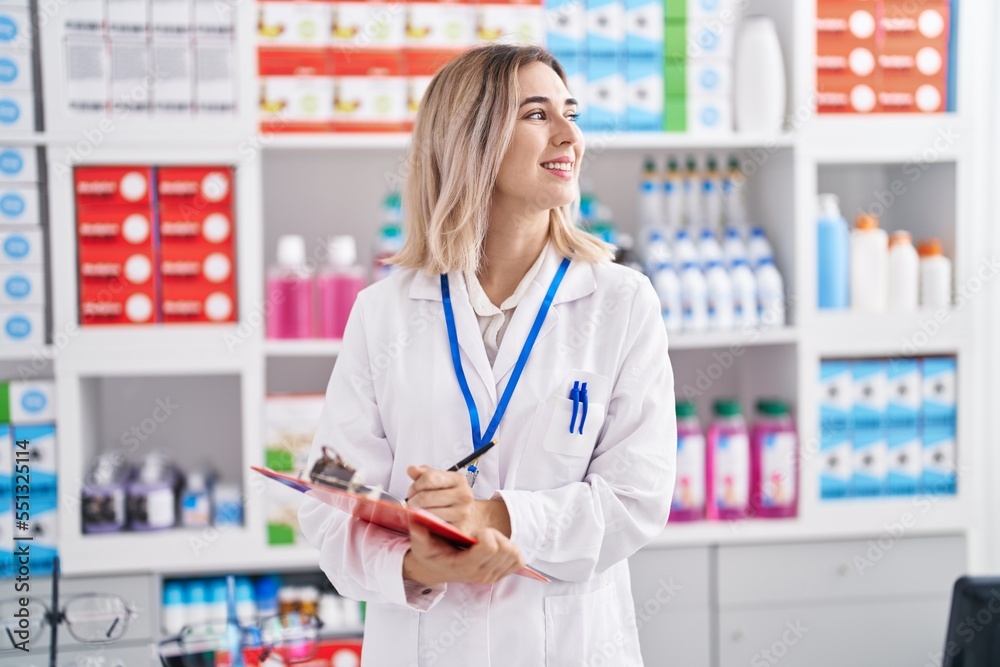 Young woman pharmacist smiling confident writing on document at pharmacy