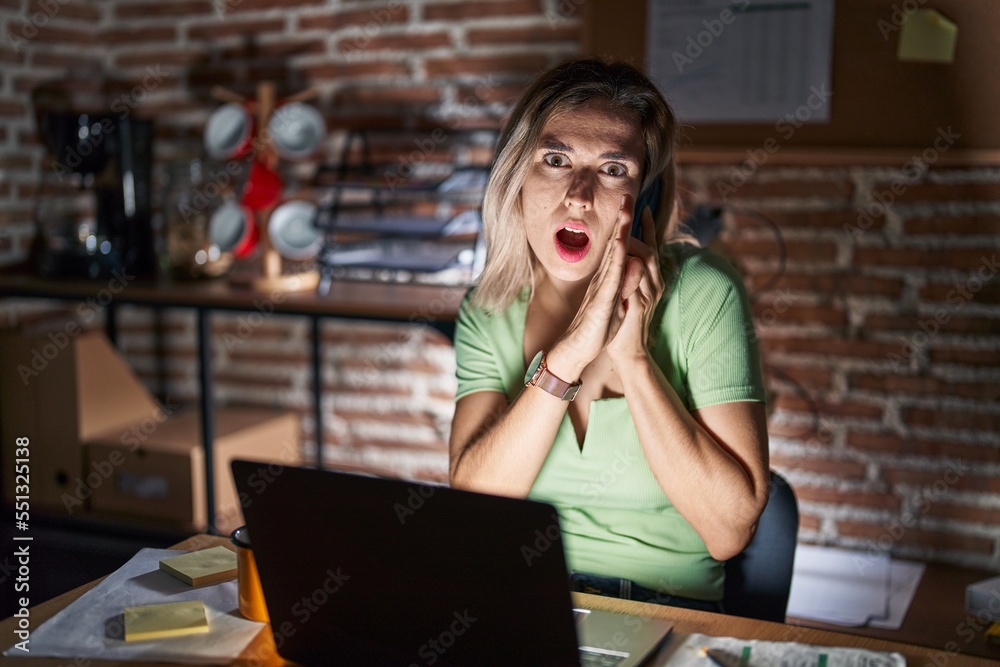 Young beautiful woman working at the office at night speaking on the phone hand on mouth telling secret rumor, whispering malicious talk conversation Young beautiful woman working at the office at night speaking on the phone hand on mouth telling secret rumor, whispering malicious talk conversation