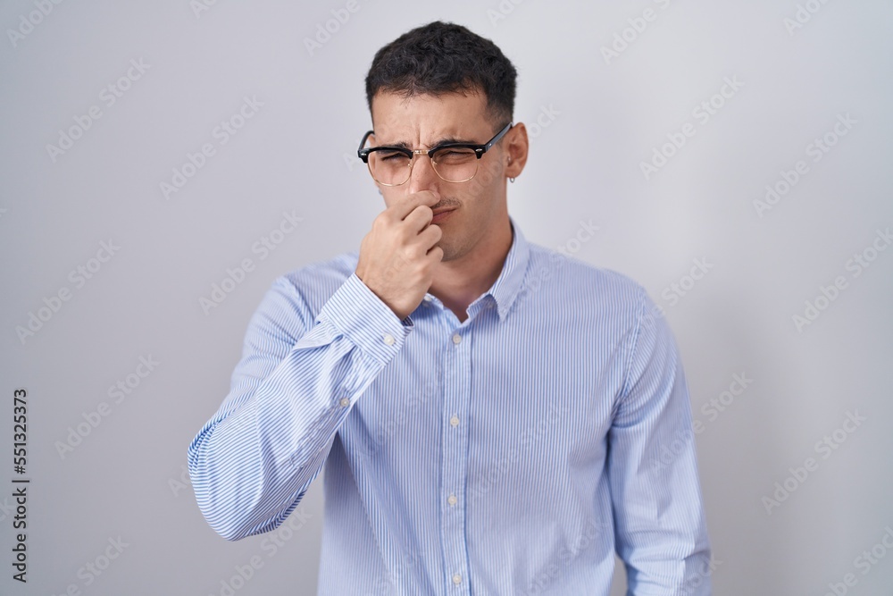 Handsome hispanic man wearing business clothes and glasses smelling something stinky and disgusting, intolerable smell, holding breath with fingers on nose. bad smell Handsome hispanic man wearing business clothes and glasses smelling something stinky and disgusting, intolerable smell, holding breath with fingers on nose. bad smell