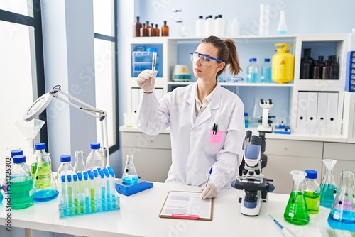 Young woman wearing scientist uniform analysing herb at laboratory