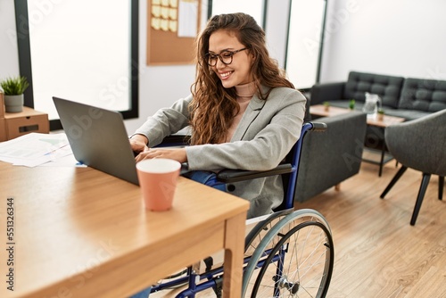 Young beautiful hispanic woman business worker using laptop sitting on wheelchair at office