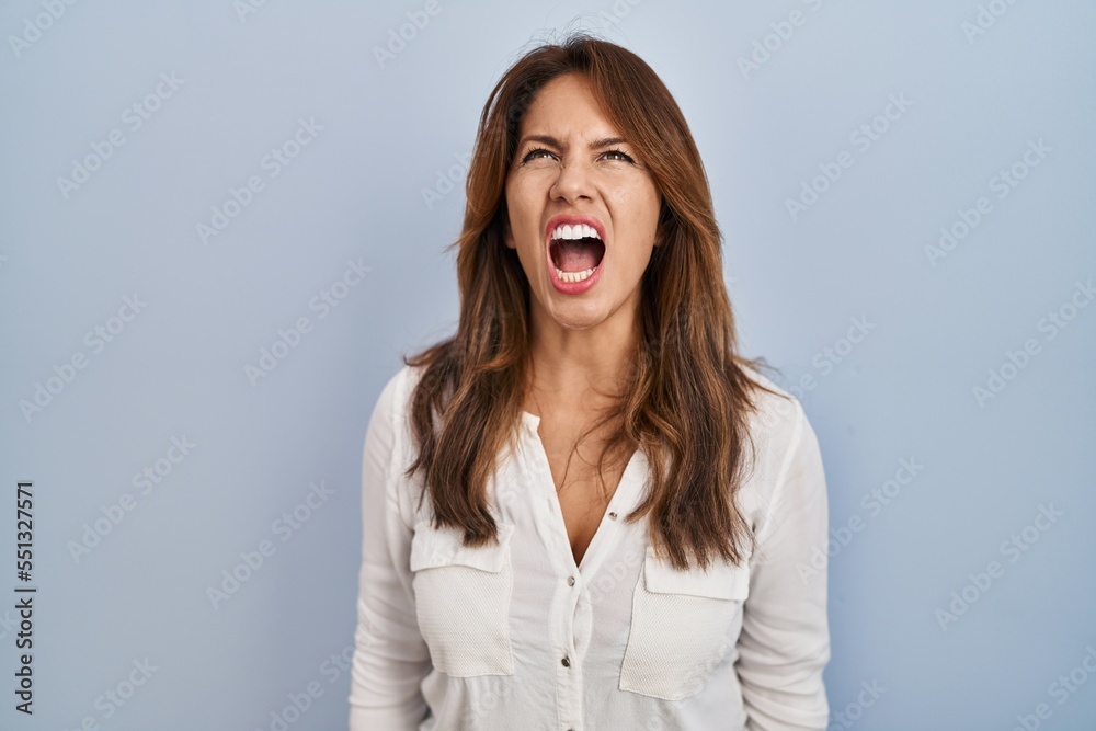 Hispanic woman standing over isolated background angry and mad screaming frustrated and furious, shouting with anger. rage and aggressive concept. Hispanic woman standing over isolated background angry and mad screaming frustrated and furious, shouting with anger. rage and aggressive concept.